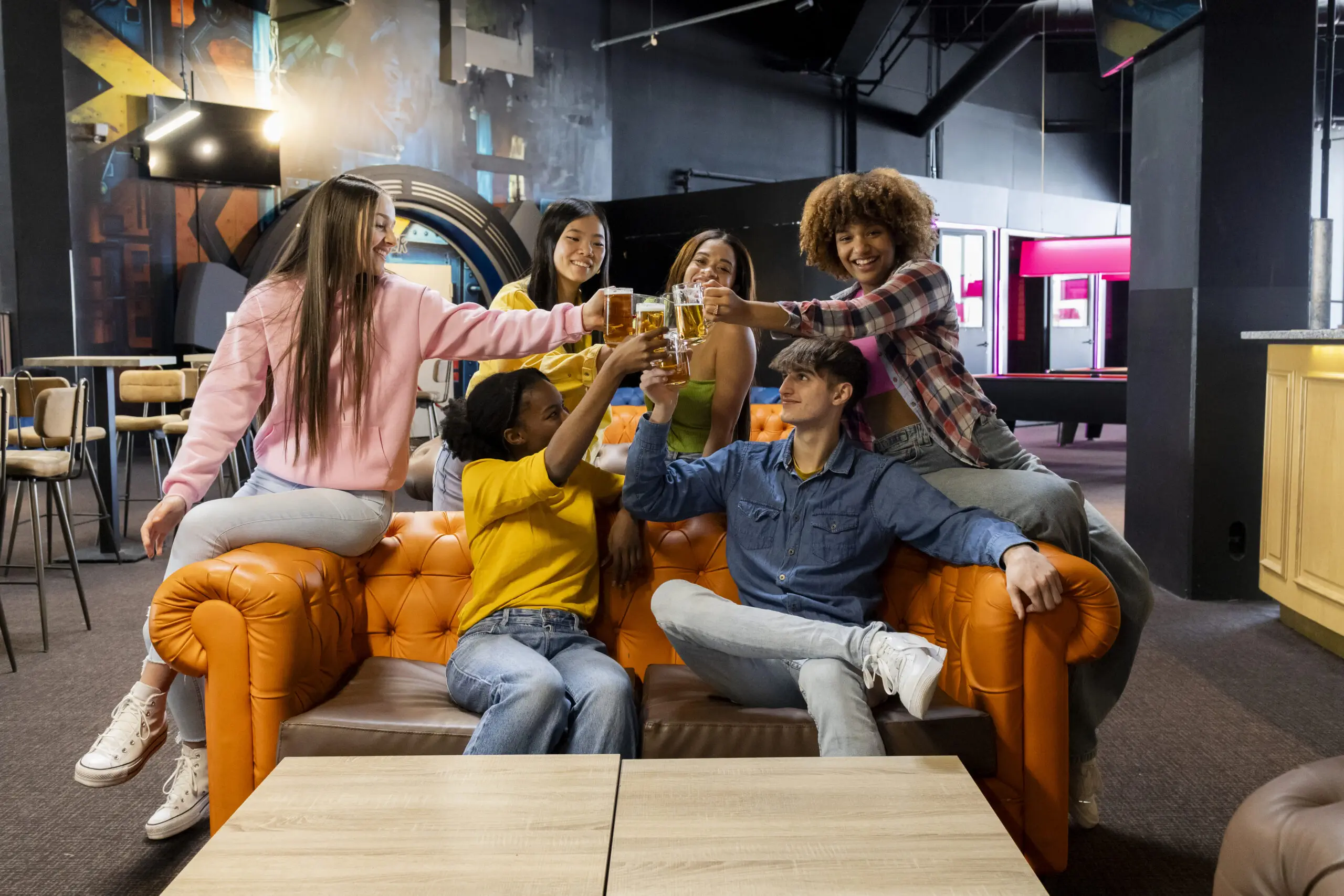 Cheerful friends toasting with beverages at a colorful arcade lounge.