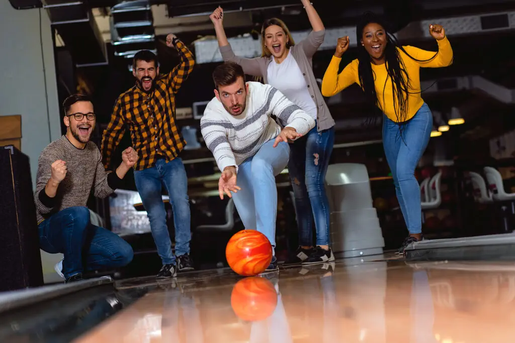 Group of friends enjoying time together laughing and cheering while bowling at club.