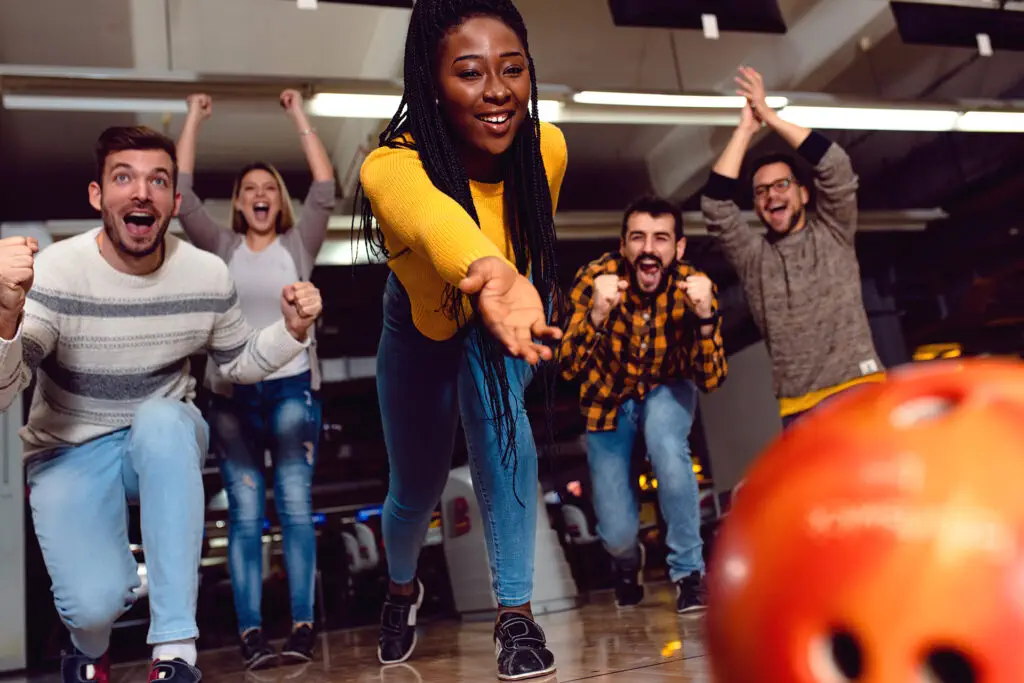 Group of friends enjoying time together laughing and cheering while bowling at club.