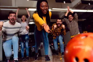 Group of friends enjoying time together laughing and cheering while bowling at club.
