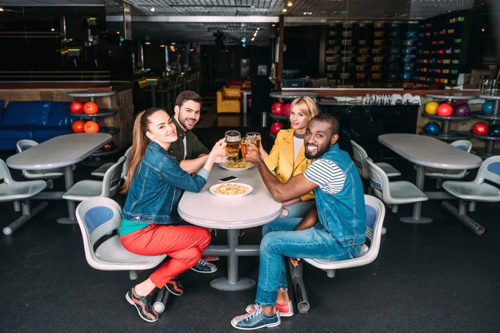 group of young friends clinking mugs of beer at bowling club